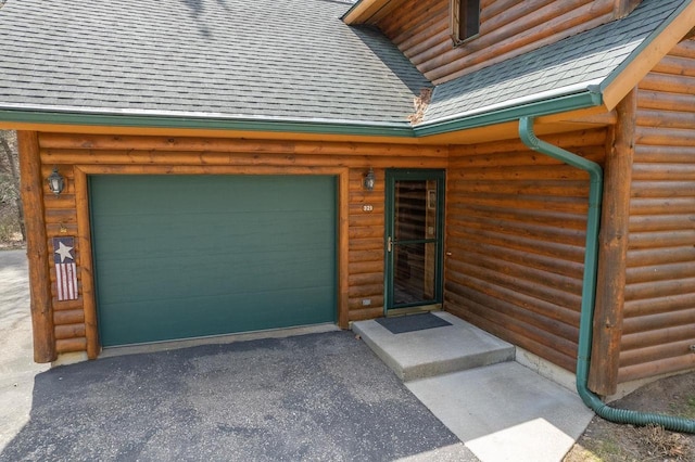 entrance to property featuring a shingled roof, a garage, and aphalt driveway