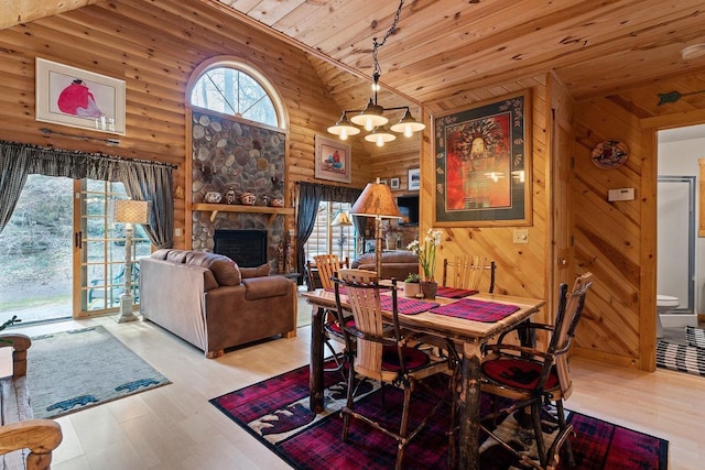 dining room featuring a chandelier, wood ceiling, wood finished floors, a stone fireplace, and high vaulted ceiling