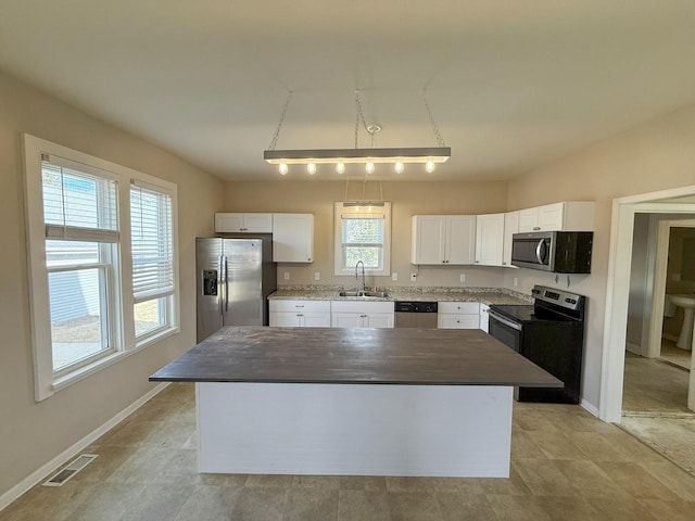 kitchen featuring stainless steel appliances, a kitchen island, a sink, visible vents, and white cabinets