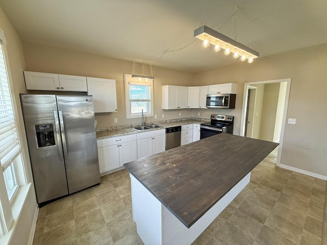 kitchen featuring appliances with stainless steel finishes, white cabinetry, a sink, and baseboards