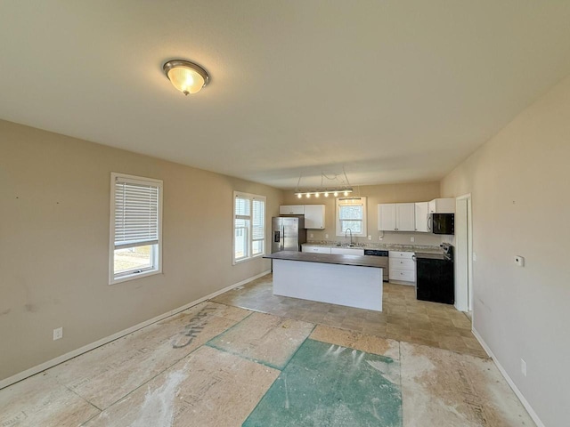 kitchen with a sink, baseboards, white cabinets, appliances with stainless steel finishes, and a center island