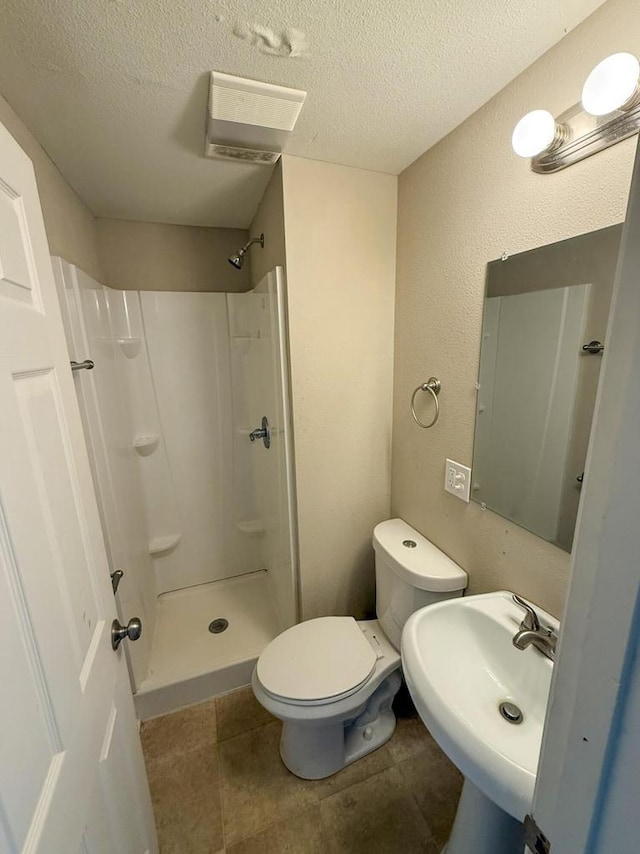 bathroom featuring toilet, tile patterned flooring, walk in shower, a textured ceiling, and a sink