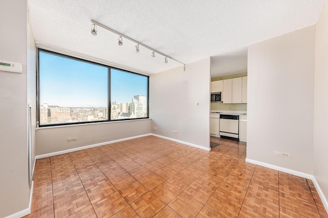 spare room featuring a textured ceiling, a city view, rail lighting, and baseboards