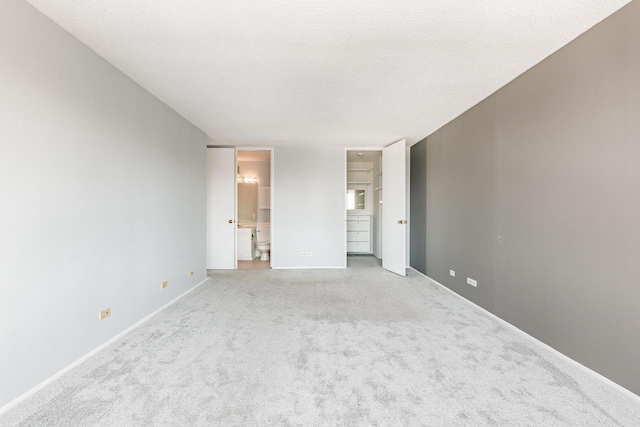 unfurnished bedroom with a textured ceiling, carpet, connected bathroom, and baseboards