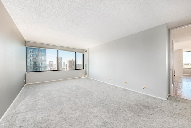 unfurnished room featuring a view of city, a textured ceiling, carpet, and baseboards