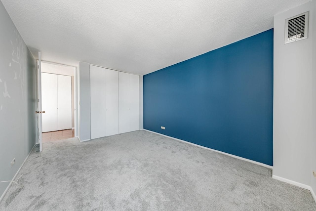 unfurnished bedroom featuring a textured ceiling, a closet, carpet flooring, and visible vents