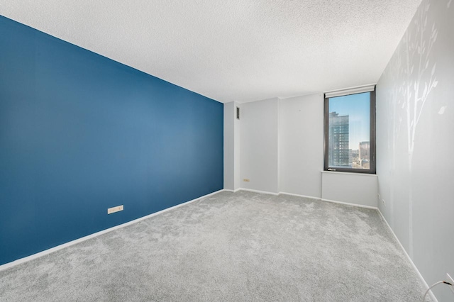 carpeted spare room with a textured ceiling and baseboards