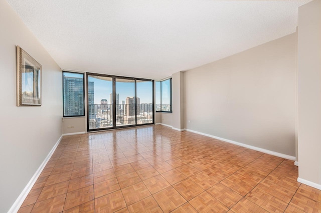 empty room featuring a view of city, floor to ceiling windows, a textured ceiling, and baseboards