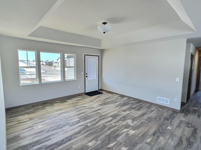 spare room featuring a tray ceiling, wood finished floors, visible vents, and baseboards