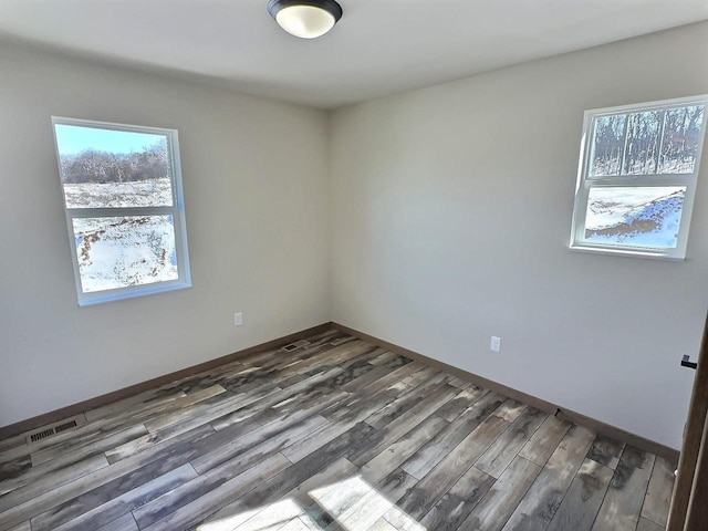 empty room with dark wood-style flooring, visible vents, and baseboards