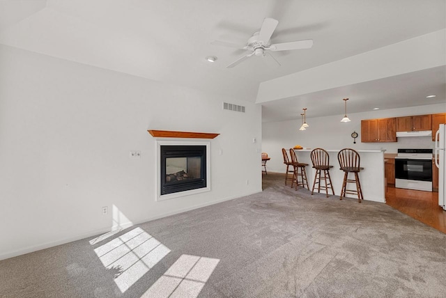 unfurnished living room with carpet floors, visible vents, a multi sided fireplace, ceiling fan, and baseboards