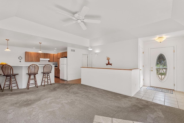 foyer entrance featuring carpet, a raised ceiling, vaulted ceiling, ceiling fan, and tile patterned floors