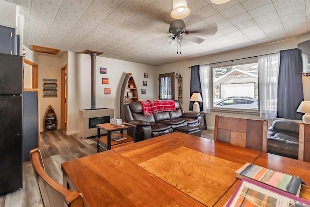 interior space with a wood stove, wood finished floors, a ceiling fan, and baseboards