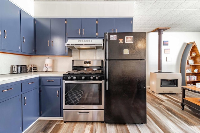 kitchen with stainless steel gas range oven, blue cabinets, under cabinet range hood, wood finished floors, and freestanding refrigerator