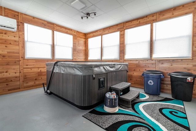 misc room featuring concrete flooring, a wall unit AC, wood walls, and a hot tub