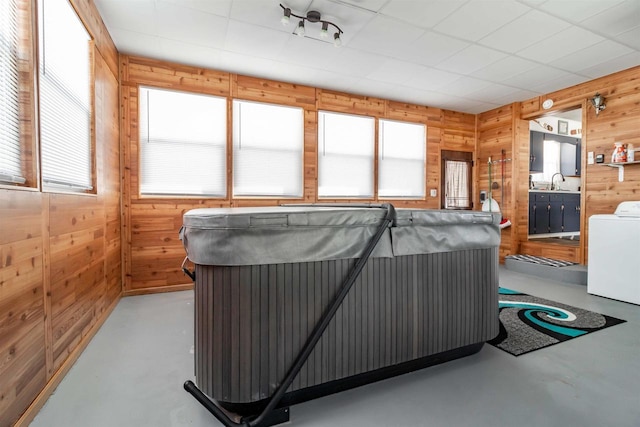 miscellaneous room with wooden walls, a hot tub, finished concrete floors, and washer / clothes dryer