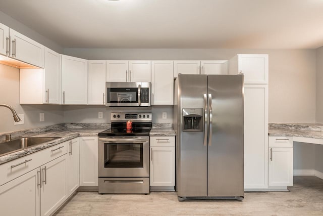 kitchen featuring appliances with stainless steel finishes, white cabinets, a sink, and light wood-style flooring