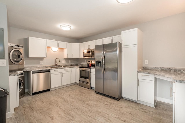 kitchen with stainless steel appliances, light wood-style floors, stacked washer / dryer, white cabinets, and a sink