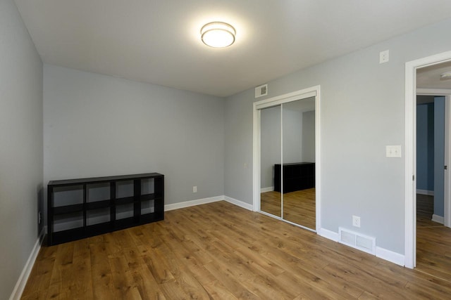 unfurnished bedroom with a closet, wood finished floors, visible vents, and baseboards