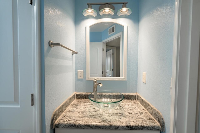 bathroom with vanity, visible vents, and a textured wall