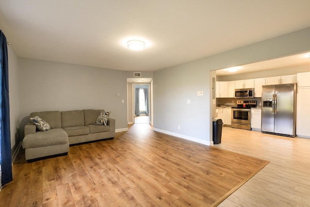 living area featuring visible vents, light wood-style flooring, and baseboards