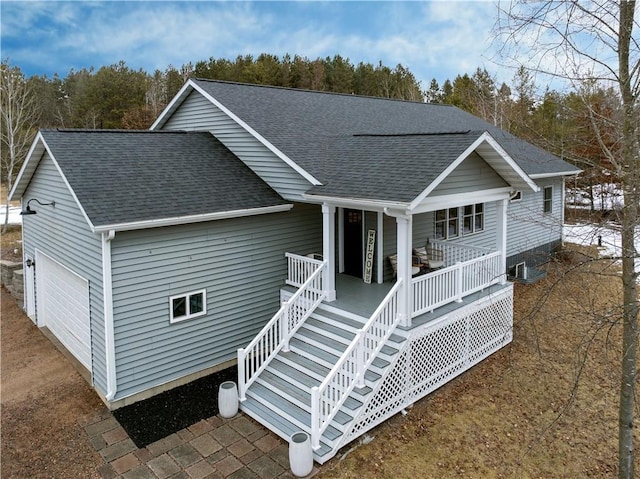 view of front of property with a garage, covered porch, and roof with shingles