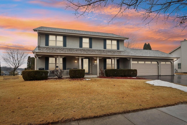 traditional-style house featuring an attached garage, aphalt driveway, a front lawn, and a porch