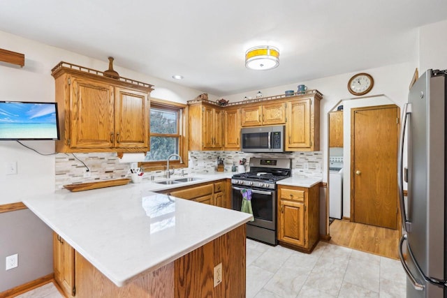 kitchen with washer / clothes dryer, light countertops, appliances with stainless steel finishes, a sink, and a peninsula