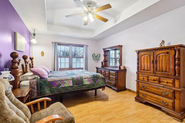 bedroom with light wood-style flooring, baseboards, a raised ceiling, and a ceiling fan