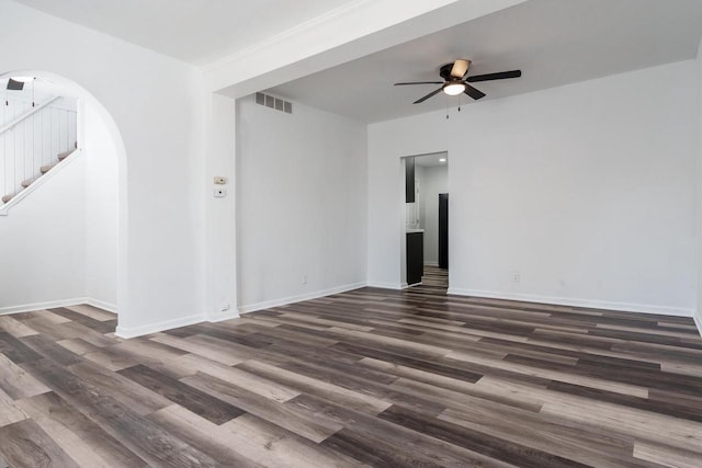 spare room with arched walkways, dark wood finished floors, visible vents, a ceiling fan, and baseboards