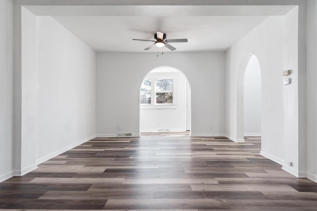 empty room featuring a ceiling fan, arched walkways, baseboards, and wood finished floors