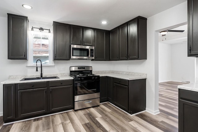 kitchen featuring appliances with stainless steel finishes, a sink, light wood finished floors, and ceiling fan