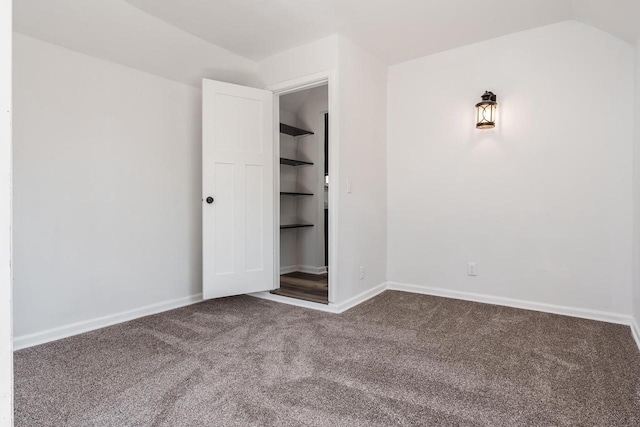 unfurnished bedroom with carpet, a walk in closet, vaulted ceiling, and baseboards