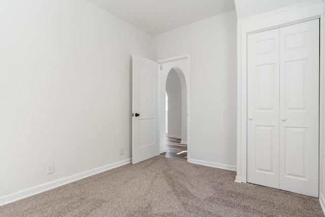 unfurnished bedroom featuring arched walkways, a closet, carpet, and baseboards