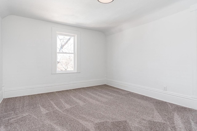 spare room featuring carpet floors, vaulted ceiling, and baseboards