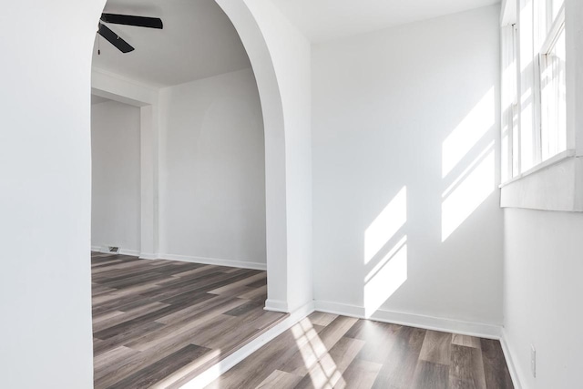 interior space featuring arched walkways, ceiling fan, baseboards, and wood finished floors