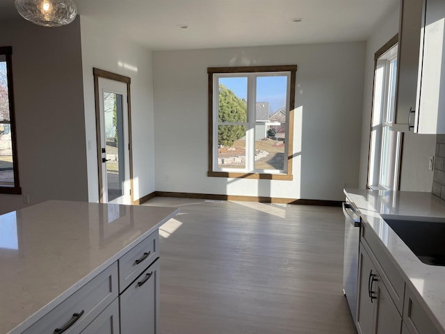 kitchen with light wood finished floors, baseboards, light stone counters, stainless steel dishwasher, and a sink