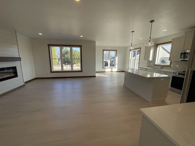 kitchen with backsplash, a center island, open floor plan, light wood-style flooring, and stainless steel appliances