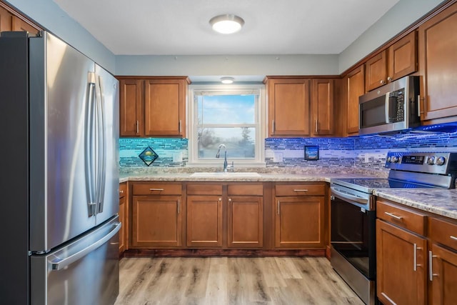 kitchen featuring brown cabinetry, decorative backsplash, light wood-style flooring, stainless steel appliances, and a sink