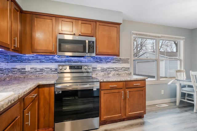 kitchen with light wood-style floors, appliances with stainless steel finishes, brown cabinetry, and decorative backsplash