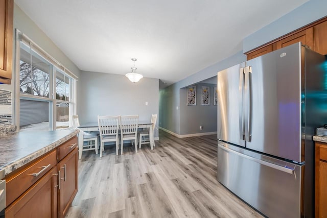 kitchen with light wood-style flooring, brown cabinetry, freestanding refrigerator, and baseboards