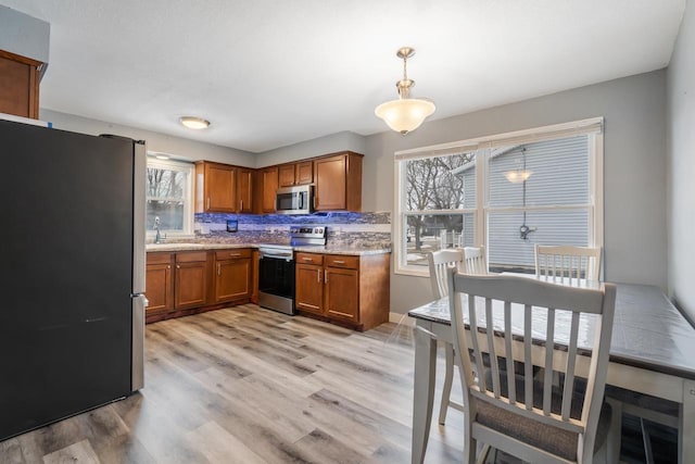 kitchen with light wood-style floors, appliances with stainless steel finishes, brown cabinets, decorative backsplash, and pendant lighting