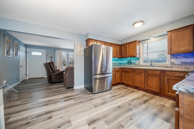 kitchen featuring a wealth of natural light, brown cabinetry, freestanding refrigerator, a sink, and light wood-type flooring