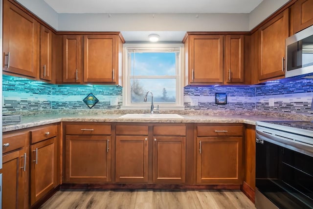 kitchen with light wood finished floors, appliances with stainless steel finishes, brown cabinets, and a sink