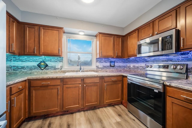 kitchen featuring light wood-type flooring, appliances with stainless steel finishes, brown cabinets, and a sink