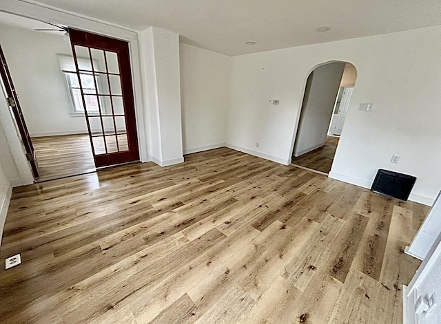 empty room with arched walkways, baseboards, and wood finished floors