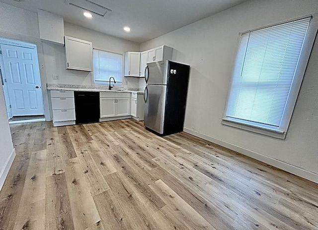 kitchen featuring black dishwasher, light countertops, freestanding refrigerator, a sink, and light wood-type flooring