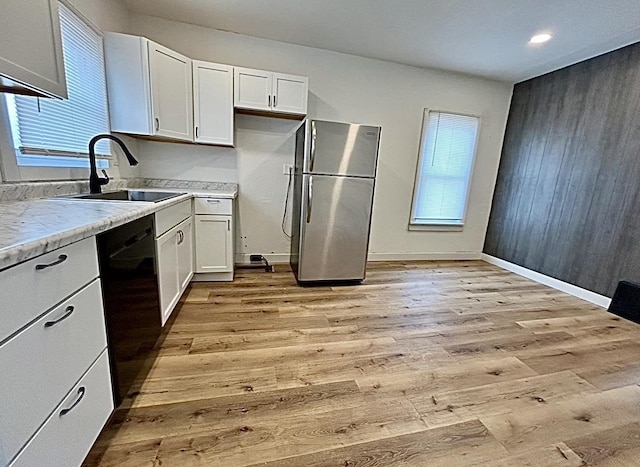 kitchen featuring light wood finished floors, black dishwasher, a sink, and freestanding refrigerator