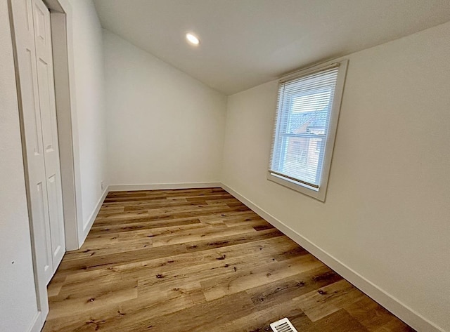 empty room featuring lofted ceiling, hardwood / wood-style flooring, baseboards, and recessed lighting