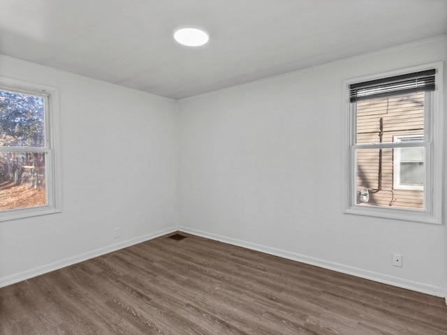 unfurnished room with dark wood-style flooring, visible vents, and baseboards